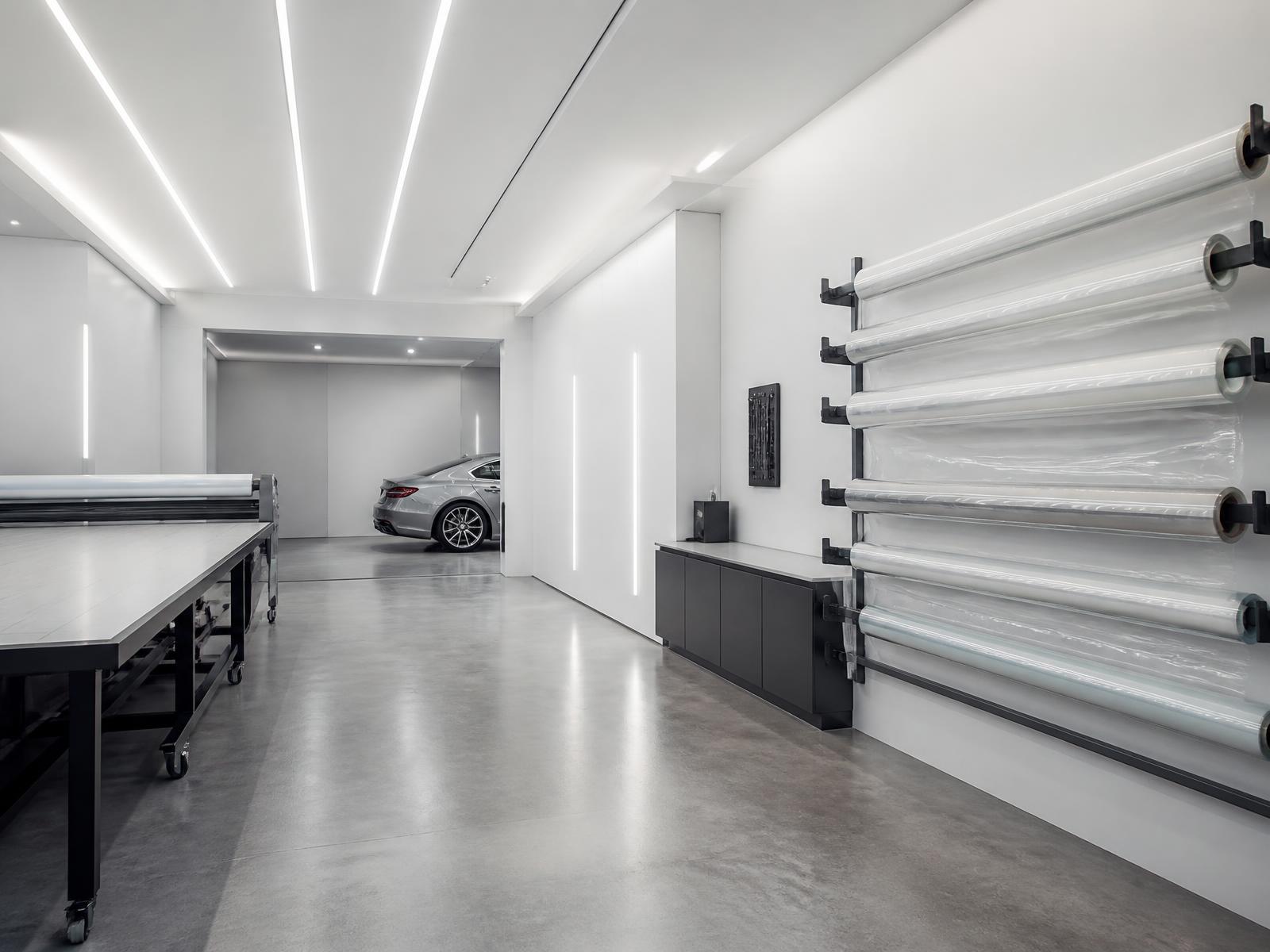 Cascade's Calgary bay: rolls of protection film on the wall rack, plotter table, and a silver sedan under the lights